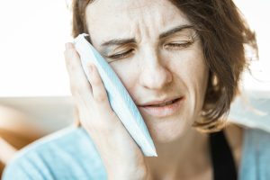 a dental patient using cold compress on the outside of cheeks because she is feeling unbearable tooth pain